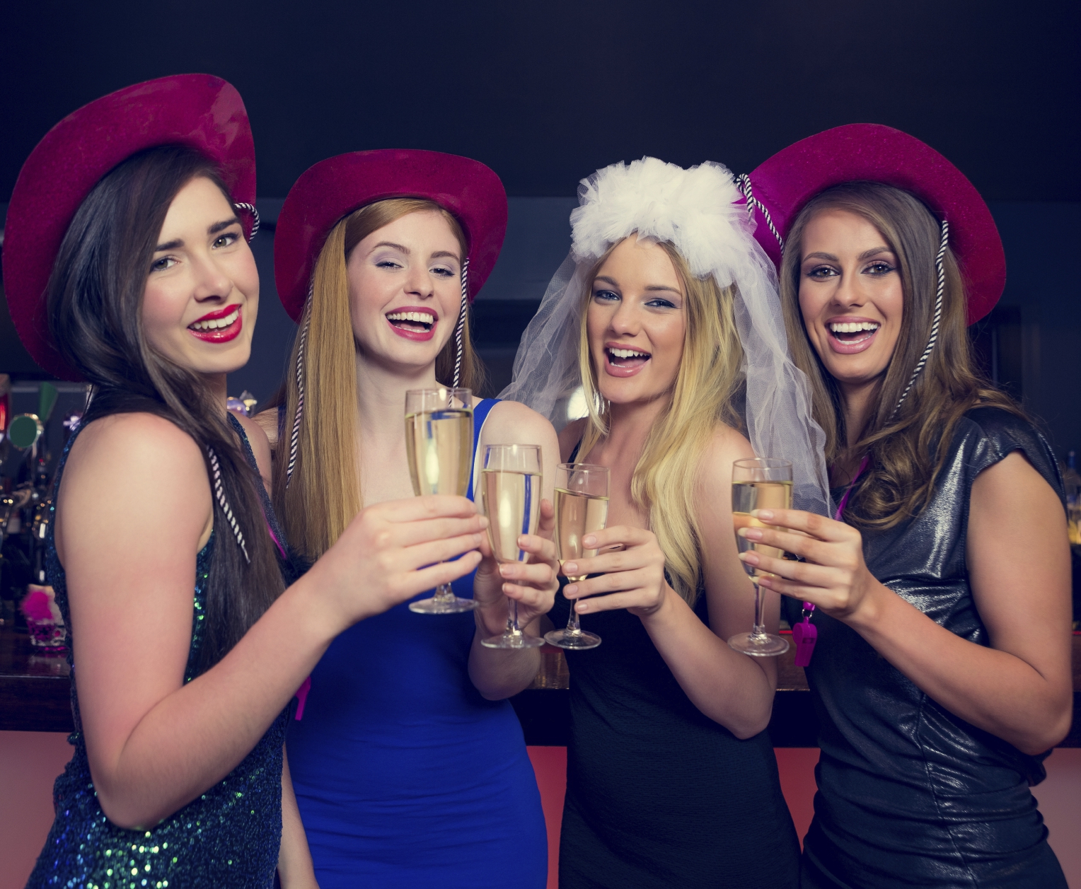 Laughing friends clinking champagne glasses at a hen night looking at camera